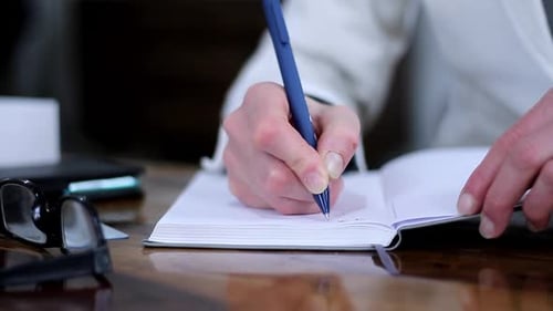 Hands Writing in Notebook at Desk