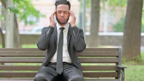 Stressed Young Adult Massaging Temples on Park Bench