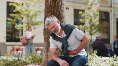Man Sits with Abdominal Pain Outdoors