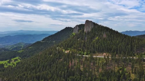 Road Passes and Meanders Among Hills Covered with Forests Against the Background of an Cloudy Sky