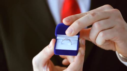 Groom holding a wedding ring box proposing marriage in a jewelry shop