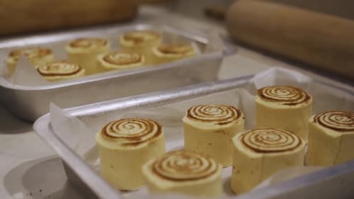 Two Trays Of Raw Cinnamon Rolls With Rolling Pins On The Background. close up