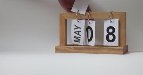 Hands Flipping Pages on Wooden Calendar, May 8th