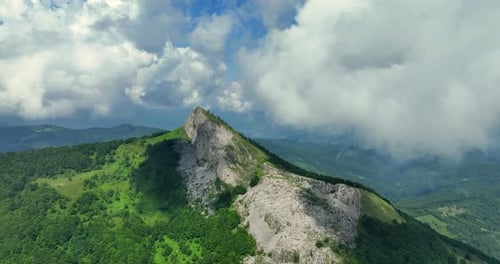 Flying trough white fluffy clouds above green mountain peaks. Beautiful summer sunny day on the high