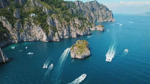 Capri Seashore with floating yachts. Dynamic waterscape with boats cruising around the iconic Faragl