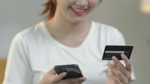 Young woman is using credit card for shopping online via application at home.
