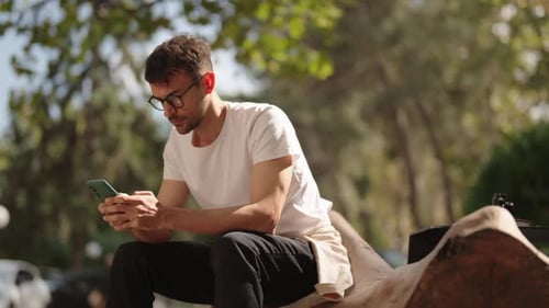 Young Man Using Phone in Park on Sunny Day