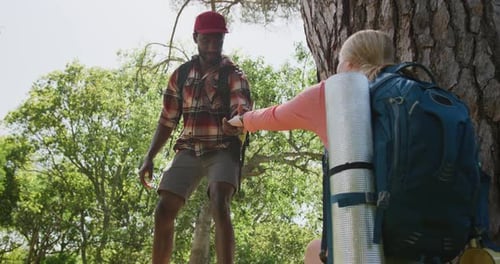 Happy diverse couple hiking with backpacks in park, slow motion
