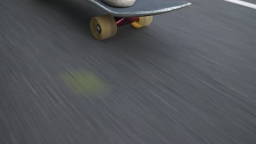 Closeup shot of downhill skateboarding in a park. Camera angle goes from three quarter view to side
