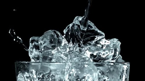 Pouring Clear Liquid Over Ice Cubes in Glass