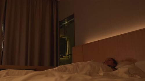 Solitary Visitor Unwinds in Dimly Lit Room Amidst City Lights An Isolated Guest Finds Solace Under