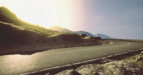 Road Winding Through Mountains Under a Bright Sunset Sky in Nature