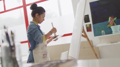 Video of biracial female artist painting in studio