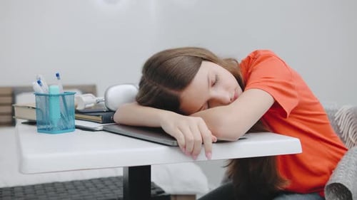 Teenage Girl Feels Exhausted While Studying at a Desk in a Modern Bedroom During the Day Overwhelmed