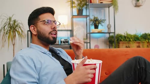 Man Relaxes on Couch Watching TV and Eating Popcorn