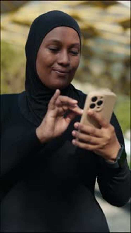 Vertical Video Smiling Muslim Female Standing After a Run and Surfing in Internet Scrolling Apps