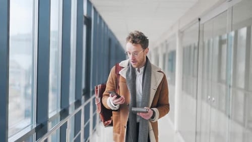 Happy adult man walking down a glass corridor receives a joyful notification on a smartphone