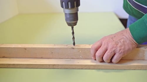Close-up of man’s hands using a cordless drill to make a hole in a wooden board