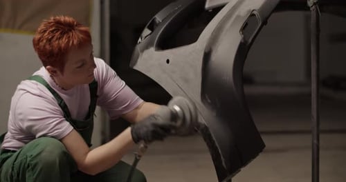 Woman Smoothing Car Bumper in Auto Repair Shop
