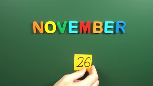 Hand sticking a sticker 26 November calendar day on school board. 26 date of November. Twenty sixth