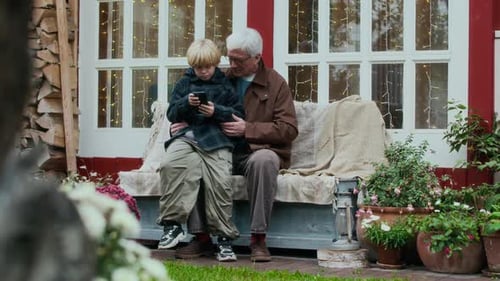 Grandfather and Grandson Sit Together Looking at Phone