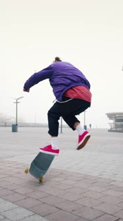 Rear View of Young Modern Guy Training His Skateboarding Skills in an Empty City Square on a Foggy