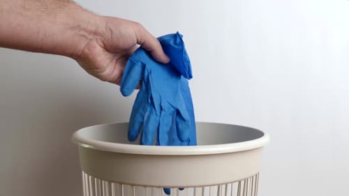 Dropping Medical Gloves into Beige Trash Bin
