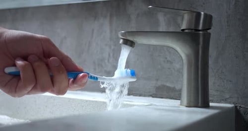 Hand Rinsing Toothbrush Under Water Cleaning Toothbrush of Toothpaste Residue Under Running Water