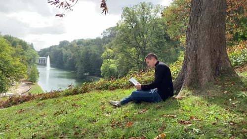 Ein Mann sitzt unter einem Baum und liest ein Buch Der Junge erlangt Wissen im Wald