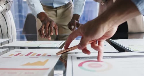Pointing at business reports and charts, team discussing project in office meeting