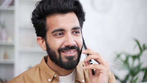 Close up. Happy young handsome man talking on smartphone while sitting in living room at home.