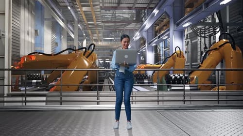 Woman Using Laptop in High-Tech Factory with Robotics