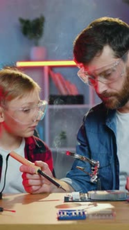 Young Boy Soldering Motherboard with Father Supervising