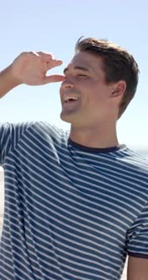 Vertical video: Smiling man enjoying sunny day at beach, wearing striped shirt