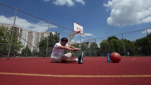 Sportive Man Doing Stretching While Sitting on Ground of Basketball Court