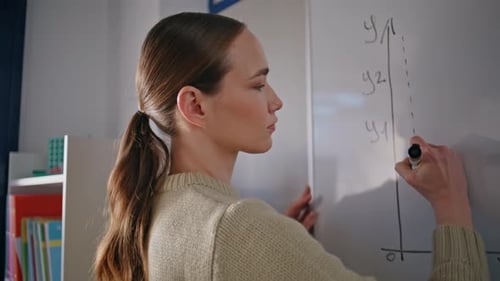 Young Woman Writes Chart on Whiteboard in Classroom