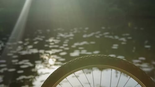 Hand Touches Bicycle Wheel Next to Water