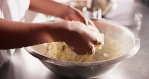Hands Mixing Dough in Stainless Steel Bowl