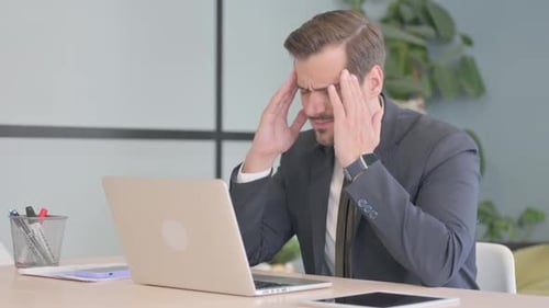 Stressed Man Rubbing Temples at Office Desk