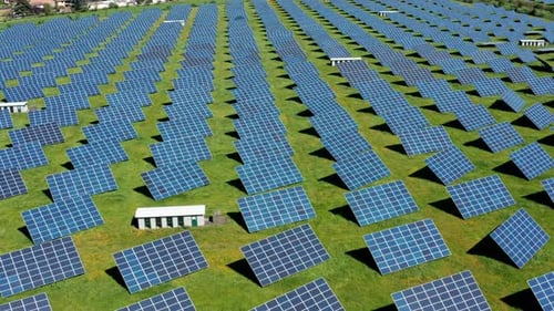 Rows of solar panels on a green field during daytime, aerial view