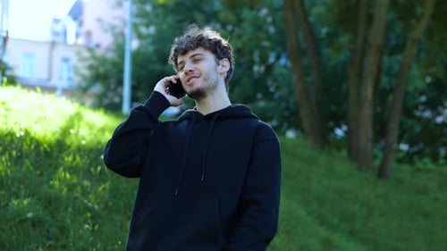 Smiling Young Man Standing in the City Park and Talking on the Mobile Phone Lifestyle Concept of
