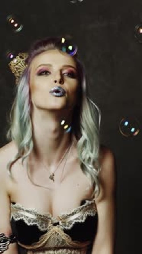 Blond blowing soap balloons. Woman posing and blowing soap bubbles on backgroung in studio