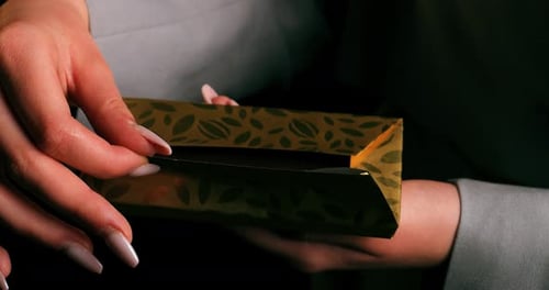 Top view of a woman's hand unwrapping and revealing a bar with golden packaging on black background