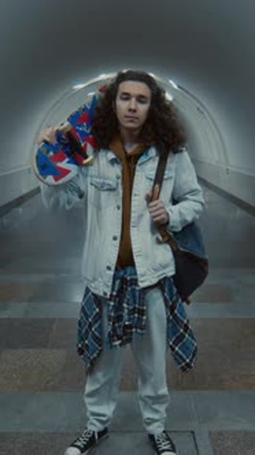 Vertical Portrait of Teenager Posing with Skateboard in Empty Tunnel