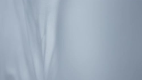 Transparente weiße seidenweiche Stoffe, die sich schnell aus einem offenen Fenster bewegen und durch das Licht hindurchscheint