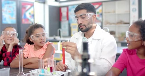 In a school classroom, a biracial teacher demonstrates a science experiment