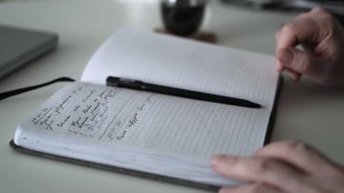 Man's hands rest by pen on notebook