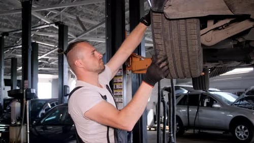 A Young Mechanic Adjusts a Tire in a Repair Shop in a Car Workshop Concentrates Lifts the Tire to a