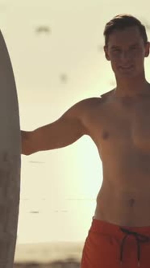 Surfer Holding Surfboard Smiling at Sunset on Beach