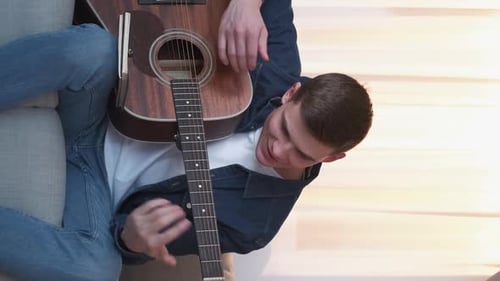 Young Man Playing Acoustic Guitar on Couch Indoors